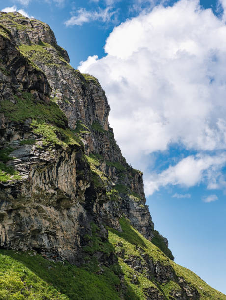 istock In Swiss Alps, rock wall with grass against blue sky with clouds 1329482346