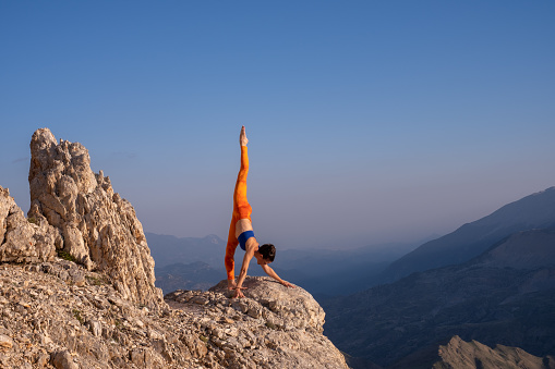 Woman practising yoga high up overlooking mountain range, on the rock.