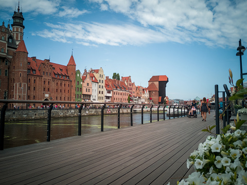 Gdańsk, Poland - July 17, 2021: Tourists walking by the Motława River in Gdańsk. At the back, there are historic houses and a port crane.