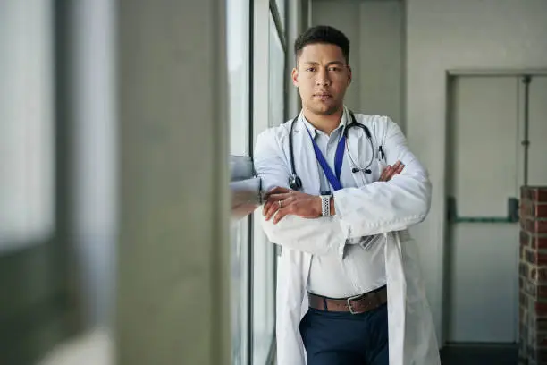 Portrait of a confident young male doctor standing with his arms crossed in the corridor of a hospital