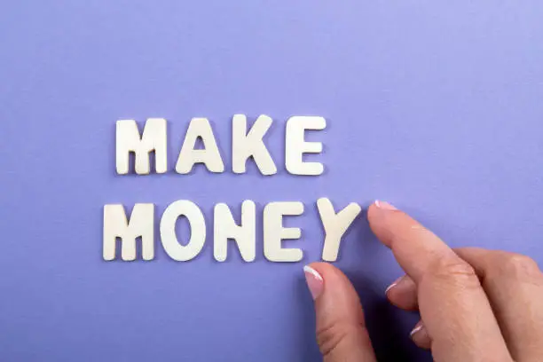 Photo of MAKE MONEY. White wooden letters on a purple background