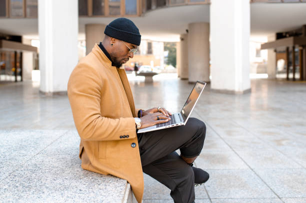 istock Elegant African man using computer laptop sitting in granite steps in metropolitan city. 1329485126