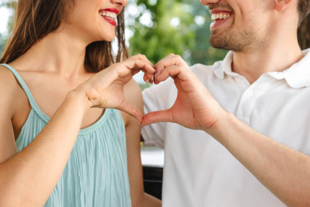 istock Loving couple sitting outdoors while showing heart love gesture. 1329485163
