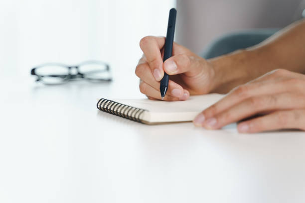 istock Close up of young man in casual cloth hands writing down on the notepad, notebook using ballpoint pen on the table. 1329485832