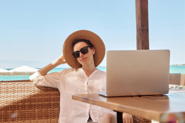 istock Young woman using laptop computer on a beach. Freelance work concept.Pretty young woman using laptop in cafe on tropical beach in outdoor cafe terrace with sea view. Work and travel 1329487317