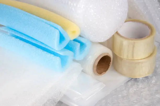 Set of plastic packaging materials - plastic stretch film rolls, foamed polyethylen sheets and rolls, transparent scotch tape, foam edge protectors, small and large bubblewrap rolls, selective focus