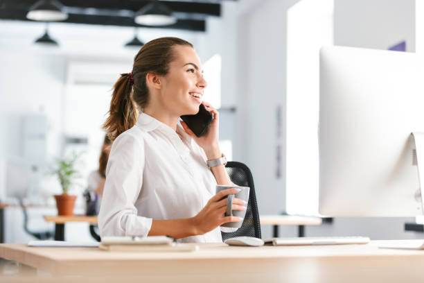 istock Cheerful business woman in office working while using computer talking by mobile phone. 1329491443