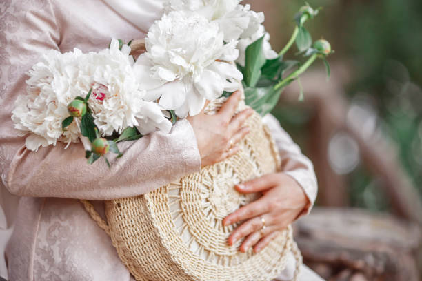A woman holds a summer hat and flowers in her hands. Close-up. stock photo