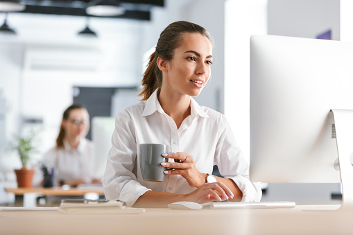 Photo of a happy cheerful business woman in office working with computer drinking coffee.