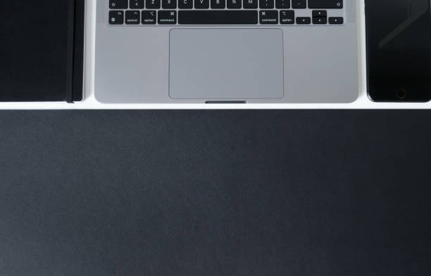 Clean modern workspace with laptop, notebook and matte black work surface on white desk