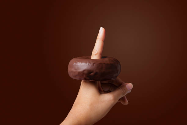 istock female hand with a chocolate donut on her finger with brown background 1329494503
