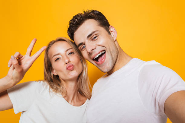 istock Loving couple standing isolated over yellow wall background take a selfie by camera. 1329495950