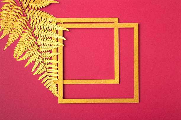 istock Minimalistic natural composition. Golden square frame and golden fern leaf on red background. Copy space 1329496073