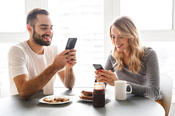 istock Loving couple sitting at the kitchen have a breakfast using mobile phones. 1329496087