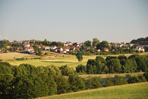 Tiny village with white houses and red roofs among green fields and meadows