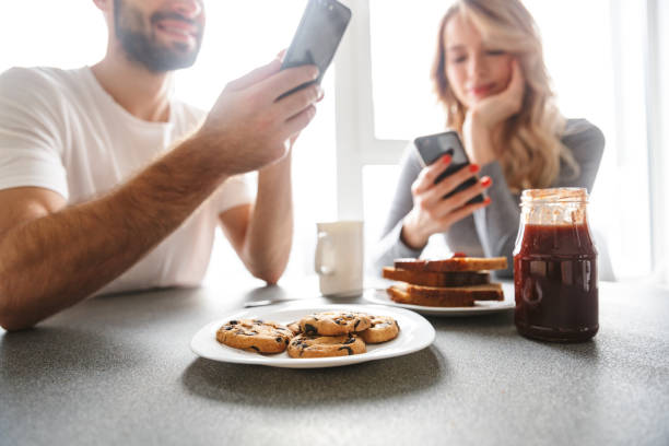 istock Loving couple sitting at the kitchen have a breakfast using mobile phones. 1329496760
