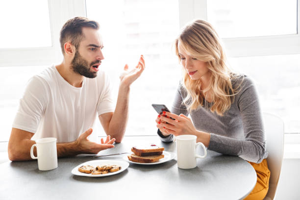 Loving couple sitting at the kitchen have a breakfast using mobile phone.