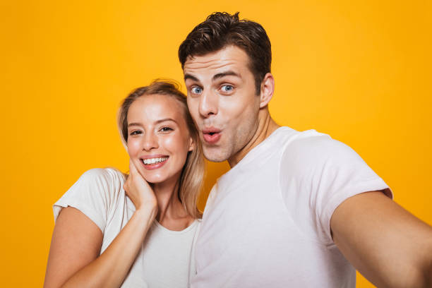 istock Loving couple standing isolated over yellow wall background take a selfie by camera. 1329496955