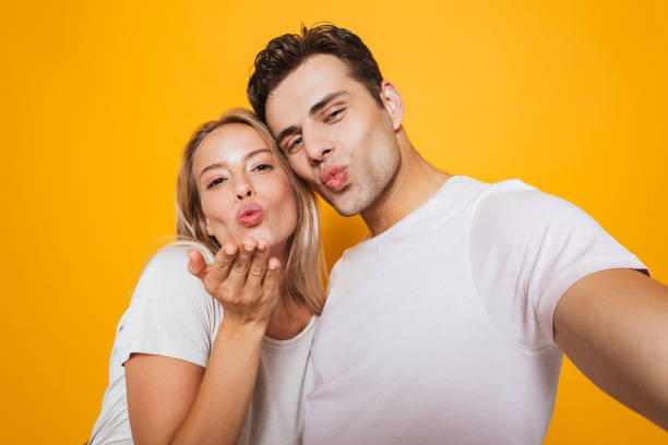 istock Loving couple standing isolated over yellow wall background take a selfie by camera. 1329497112