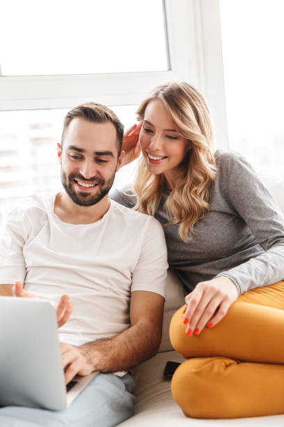 Amazing loving couple sitting indoors at home using laptop computer.