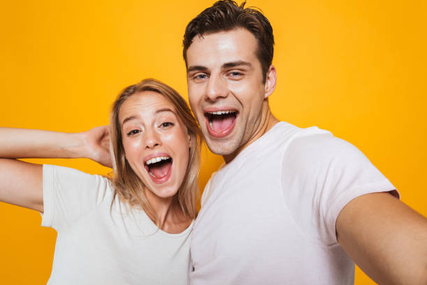 istock Loving couple standing isolated over yellow wall background take a selfie by camera. 1329497142