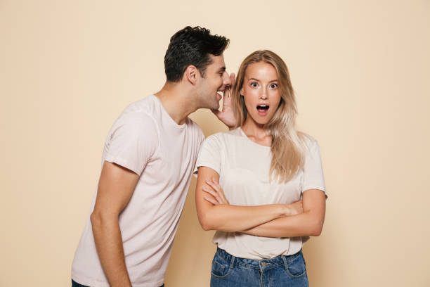 Portrait of a shocked young couple standing together Portrait of a shocked young couple standing together over beige background, telling secrets gossip stock pictures, royalty-free photos & images