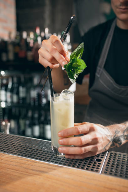 istock Cropped image of one young handsome bartender decorating an alcohol drink in tall glass enjoying his job. 1329498248