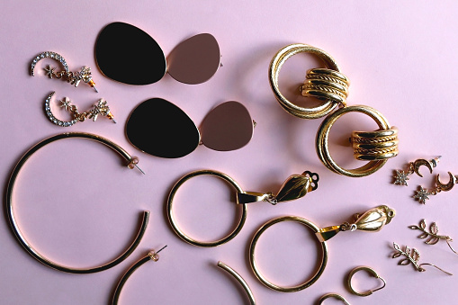 Various gold earrings on pastel pink background. Flat lay.