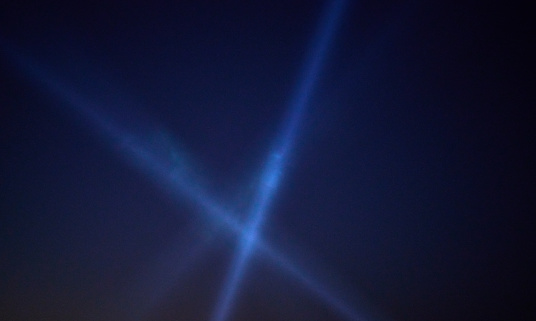 detail of a beam of white lights at a concert against a dark sky at night