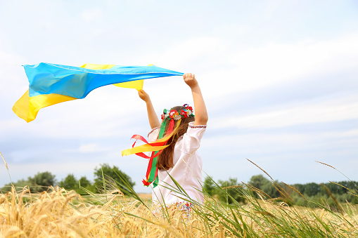 Bandera amarilla y azul de Ucrania en manos de una hermosa niña en una camisa bordada y una corona con cintas. Niño en un campo de trigo. Día de la Independencia de Ucrania, Bandera, Constitución, Bordado photo