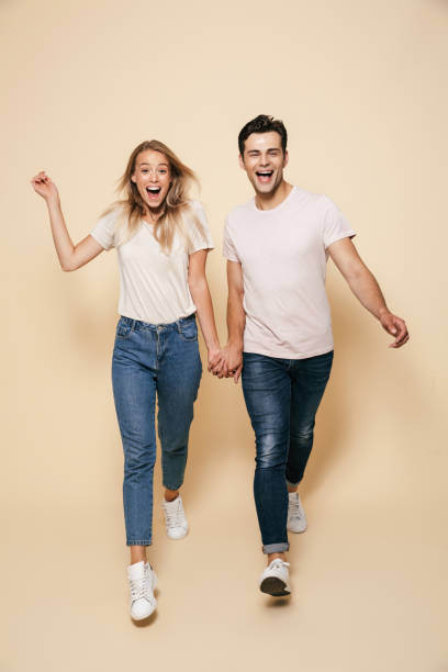 joven pareja amorosa caminando aislada sobre fondo de pared beige. - couple young women casual excitement fotografías e imágenes de stock