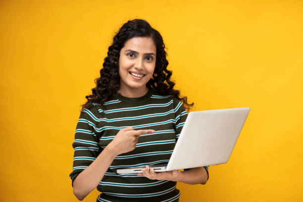 tiro de uma jovem mulher usando laptop em pé isolado sobre fundo amarelo - fashion model asian ethnicity curly hair enjoyment - fotografias e filmes do acervo