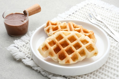 Croissant Waffle or Croffle with chocolate sauce served in plate and grey background. Selective focus image and close up.