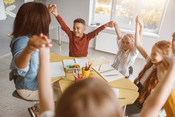 istock Children sitting at the table and raising their hands up 1329507712