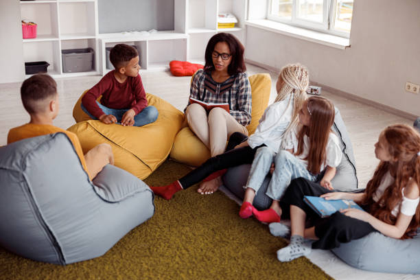 istock Teacher sitting on a pouf and reading for schoolchildren 1329507762