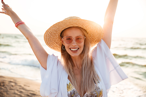 Close up of a pretty young girl in summer hat and sunglasses at the beach looking at camera, having fun