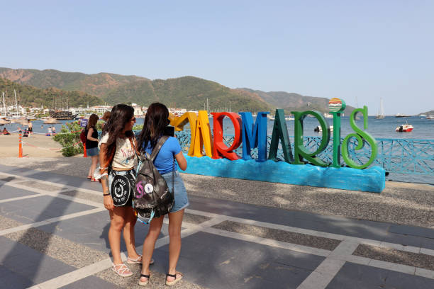 Girls tourists near the inscription Marmaris on the town embankment Marmaris, Turkey - July 2021: Girls photograph inscription Marmaris on the town embankment. View of the harbour with yachts and beach of the Marmaris yacht selfie stock pictures, royalty-free photos & images