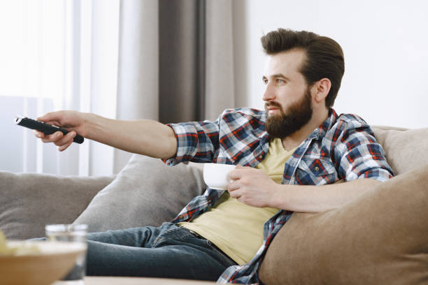 istock Man drinking coffee and watching TV on couch 1329510463