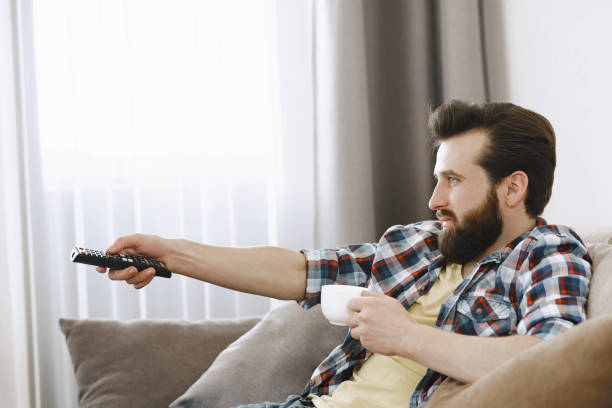 istock Man drinking coffee and watching TV on couch 1329510465