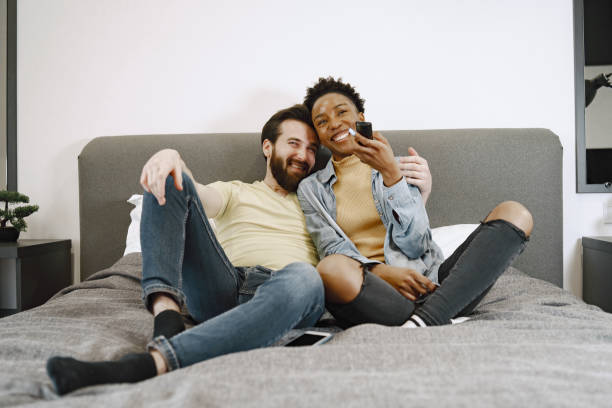 istock Multiracial pair watching tv together in bed 1329510498