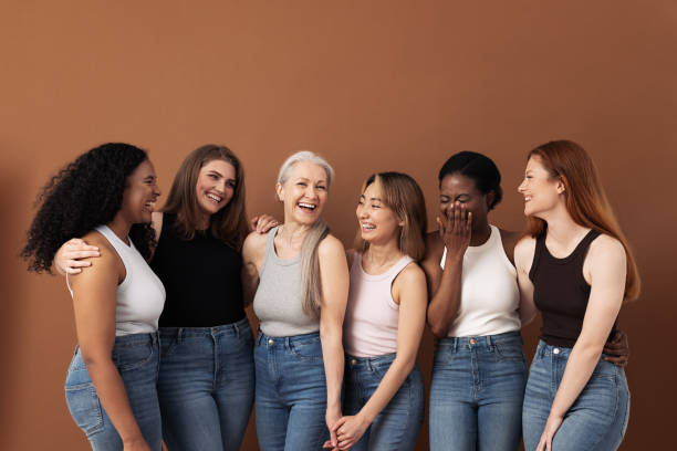 mujeres elegantes de diferentes edades divirtiéndose mientras usan pantalones vaqueros y camisetas sobre fondo marrón - human age fotografías e imágenes de stock