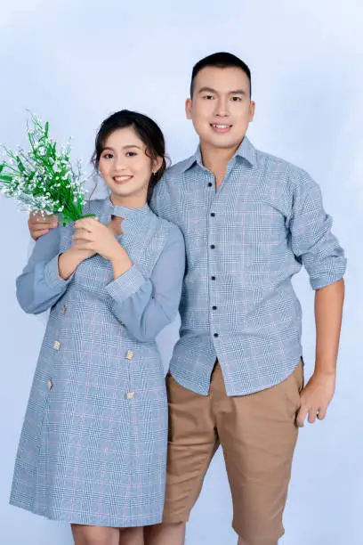 Pre-wedding portrait of a young Asian couple dressed in the same blue tones, happily posing for each other's expressions of love against a white background.