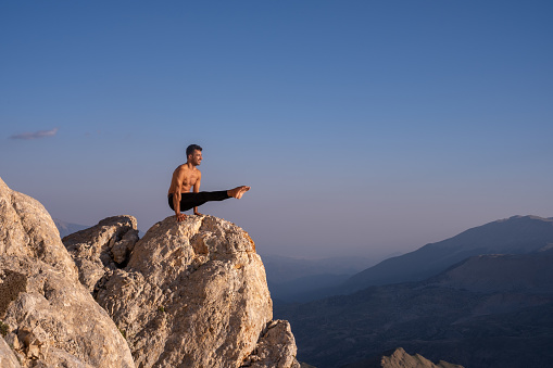 Shirtless man doing yoga on the mountain.