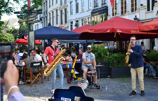 Brussels, Belgium - July 17, 2021: Agora square. 2 Russian saxophonists, drummer playing music for tourists near Grand-Place Brussels.In front music equipment cover where people can throw some money in.