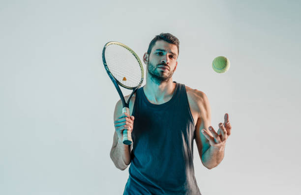 теннисист держит ракетку и подбрасывает мяч - sportsman front view studio shot looking at camera стоковые �фото и изображения
