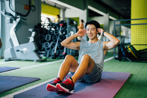 Asian young man doing sit ups in gym.