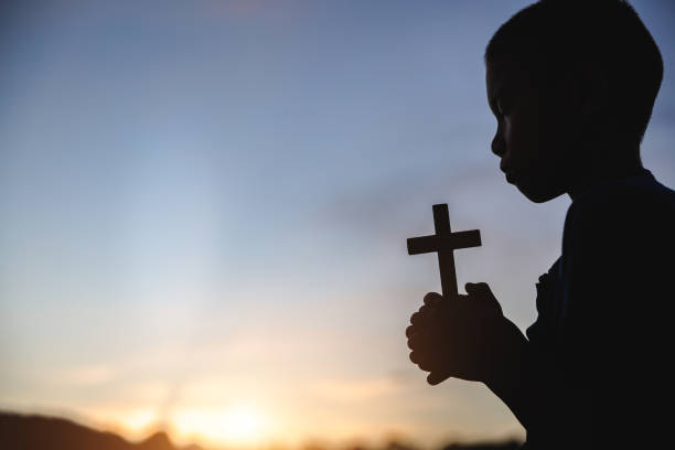 silhouette des betenden kindes mit kreuz in der natur sonnenaufgang hintergrund, kruzifix, symbol des glaubens. christliches lebenskrisengebet zu gott. - praying god love wisdom stock-fotos und bilder