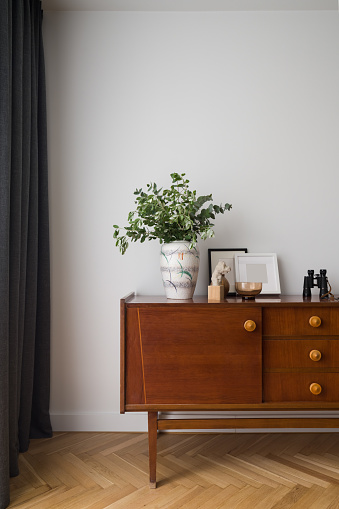 Retro, wooden cupboard with small drawers and stylish decorations in room with wooden floor