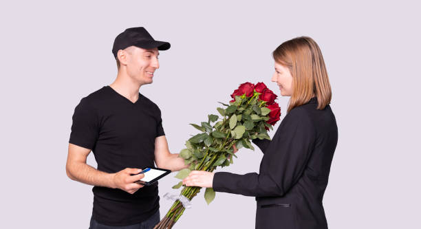 kobieta biznesu dostała bukiet kwiatów od kuriera w czarnym mundurze i musi podpisać się pod dostawą. - digital tablet young men women short hair zdjęcia i obrazy z banku zdjęć