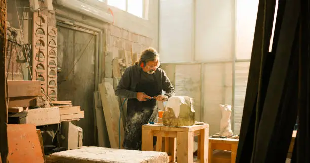 Photo of Stonemason carving stone with an electric chisel in his studio